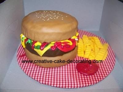 A hamburger shaped cake on a checked cake board.