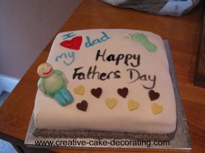 A square white cake with heart deco and a human figurine topper