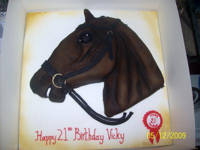 A 2d horse face cake decorated in brown icing. Cake is on a square gold cake board.
