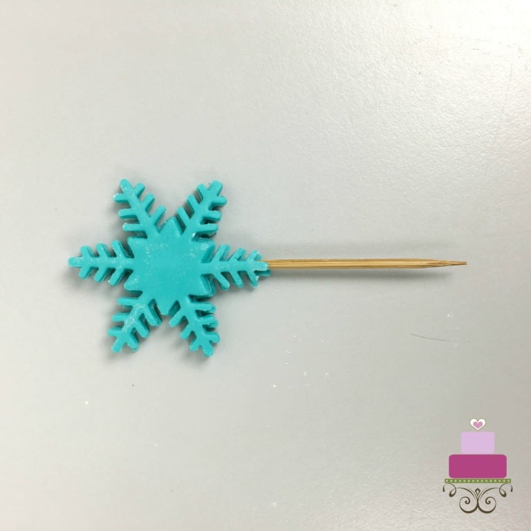 A snowflake fondant cut out with a toothpick attached