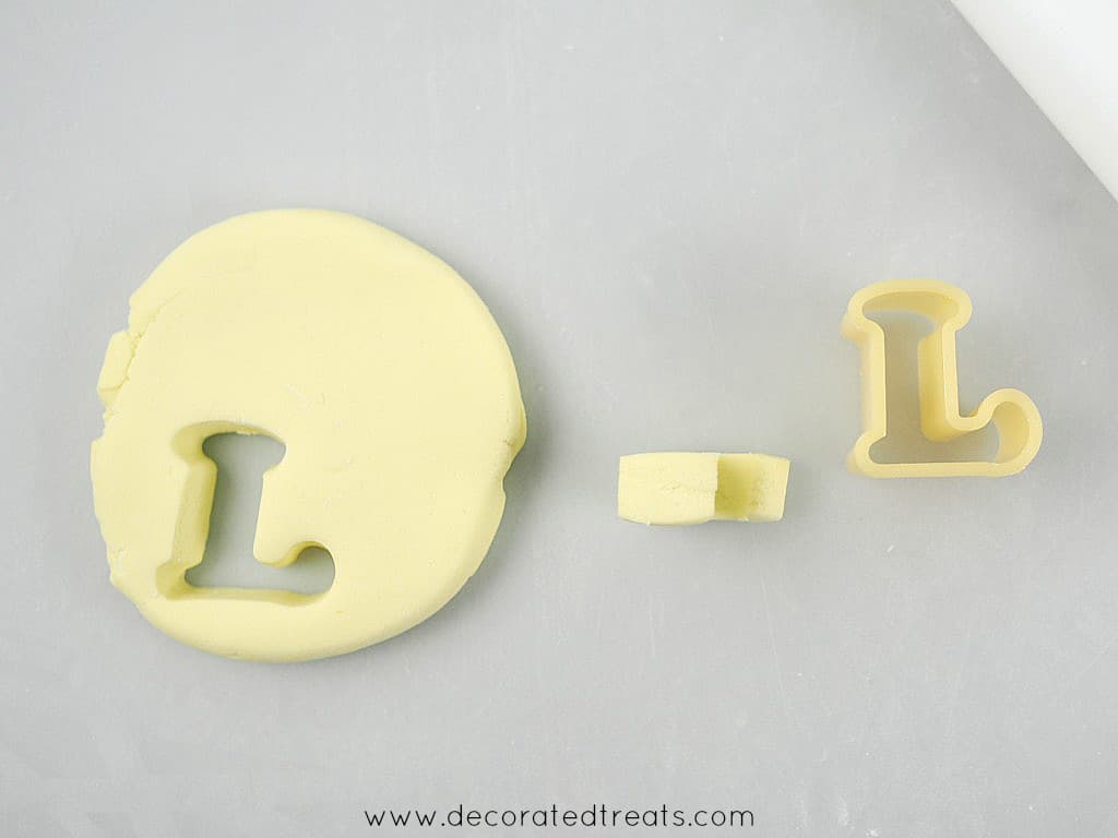 A thick rolled fondant, with a letter L cut out of it. In the background is letter L cutter