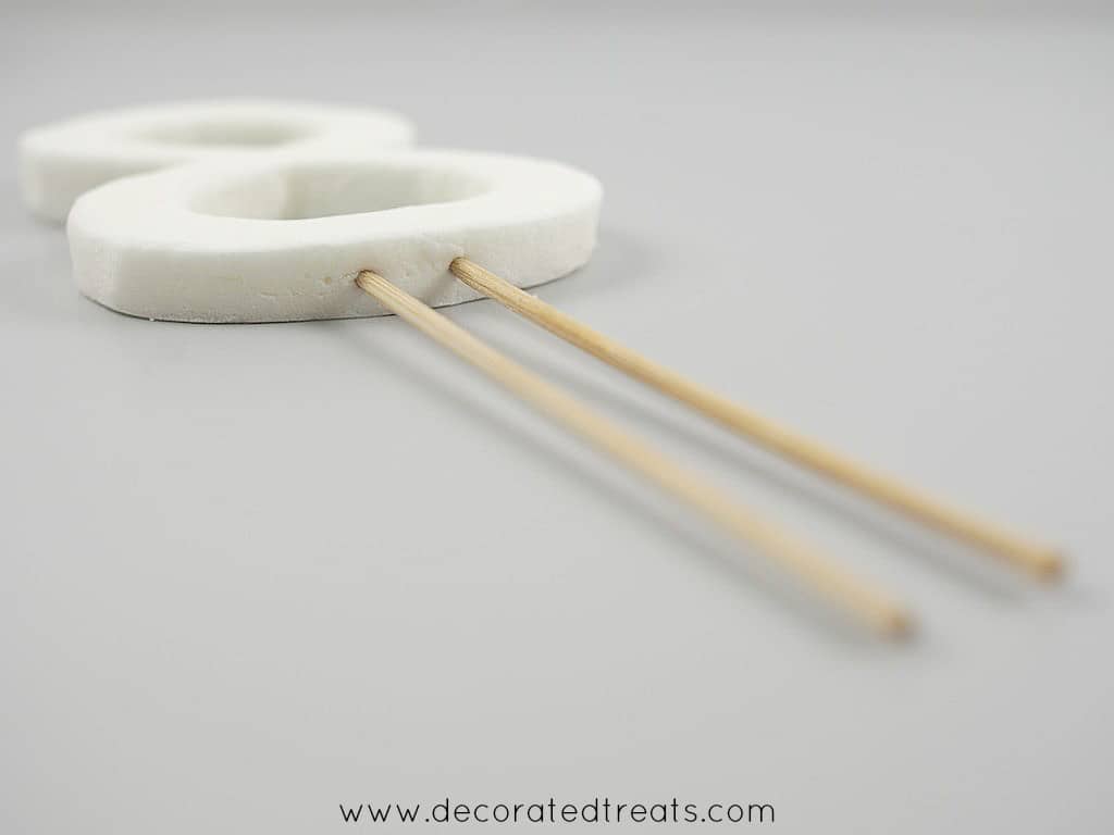 A number 8 shaped fondant cut out in white, attached to 2 long picks