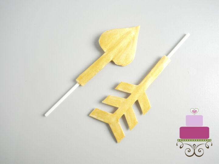 Gold painted gum paste arrow attached to white lollipop sticks.