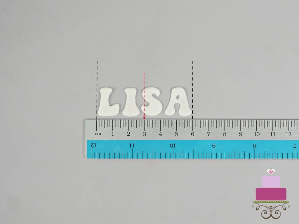 Alphabets L, I, S and A in white fondant. A ruler is used to measure the length of the name.