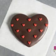 A heart shaped cookie covered in chocolate and decorated with tiny fondant hearts.