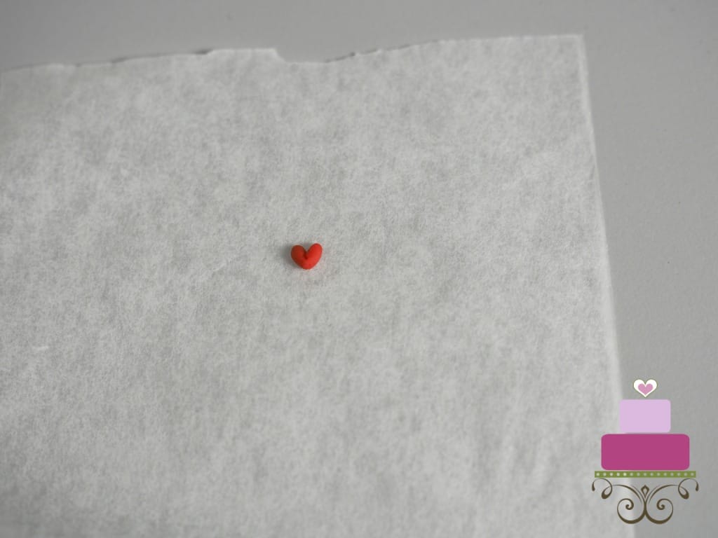 Tiny red fondant heart on a parchment paper.