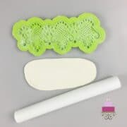 Green silicone fondant mold, some rolled white fondant and a small rolling pin.