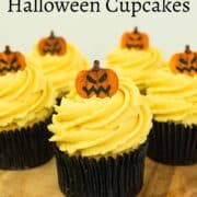 Cupcakes in black liners with pumpkins toppers, on a brown cake stand.