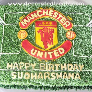 A rectangle cake decorated with green buttercream grass and a large Manchester United football club logo.