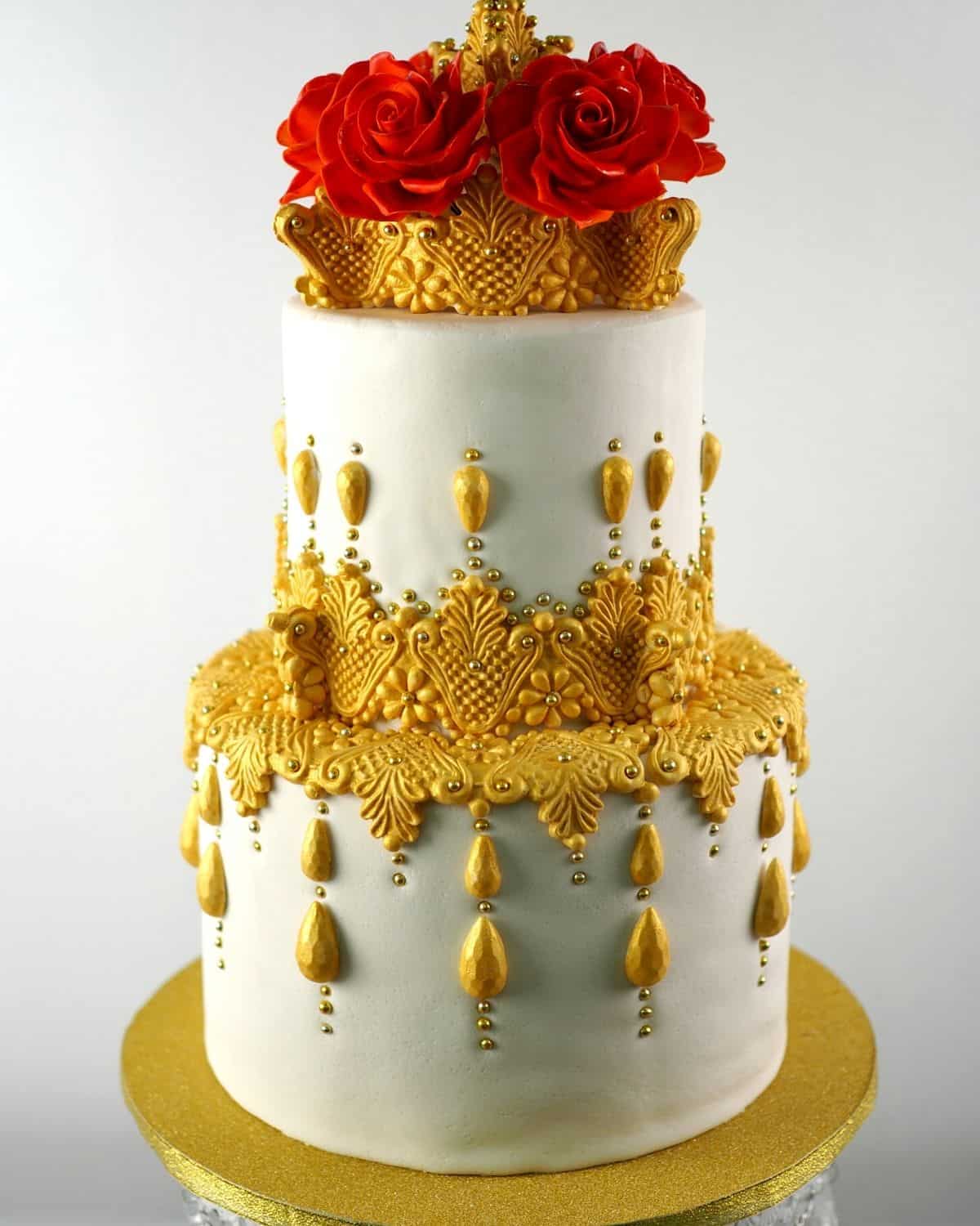 A white cake decorated with gold painted molded fondant and gold dragees