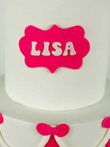 Name 'LISA' on a pink plaque on a white fondant cake