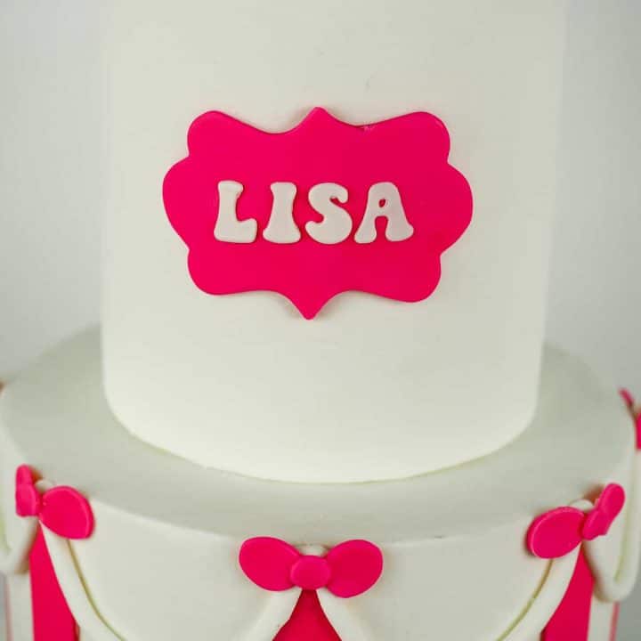Name 'LISA' on a pink plaque on a white fondant cake