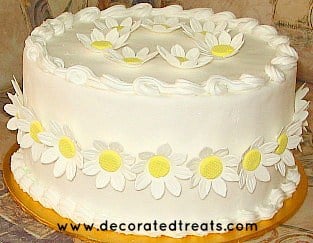 A round white cake decorated with fondant daisies