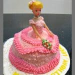 Doll cake in pink buttercream gown, with the doll holding a bouquet of buttercream flowers.