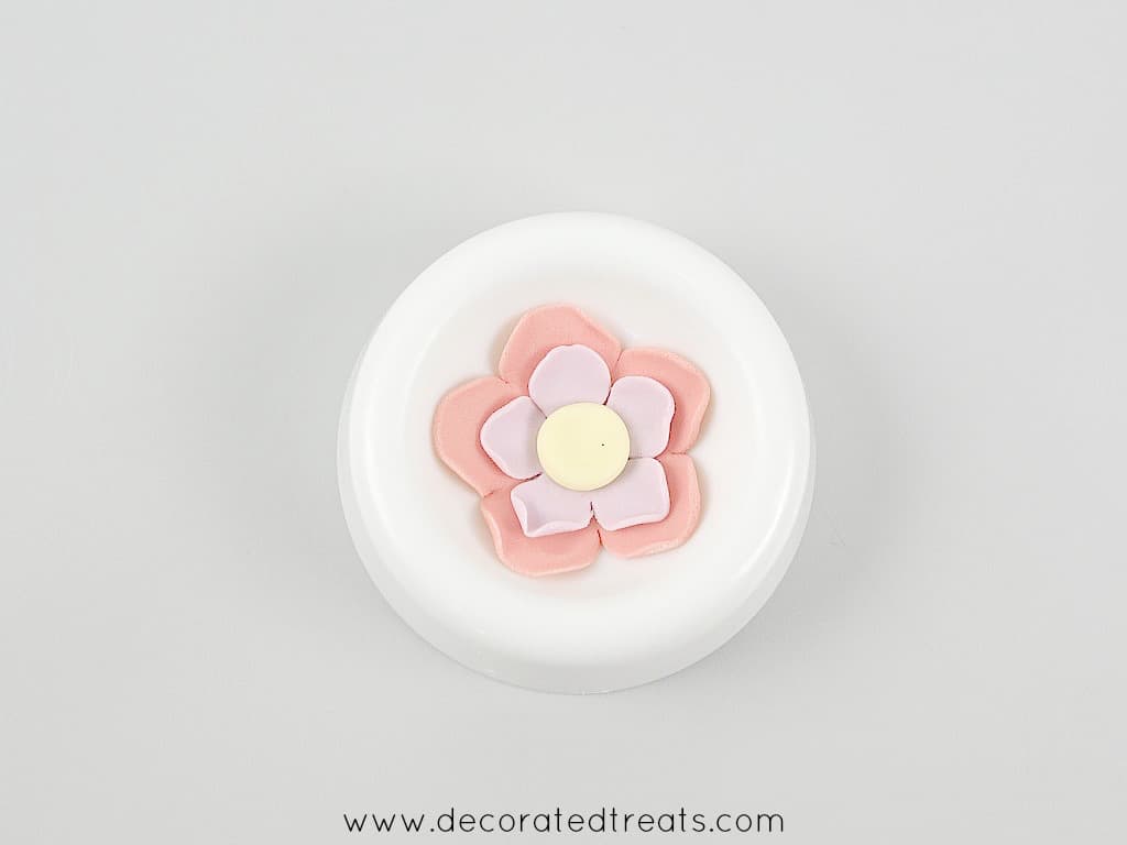A pink and purple 5 petal fondant flower with a yellow center in a flower former
