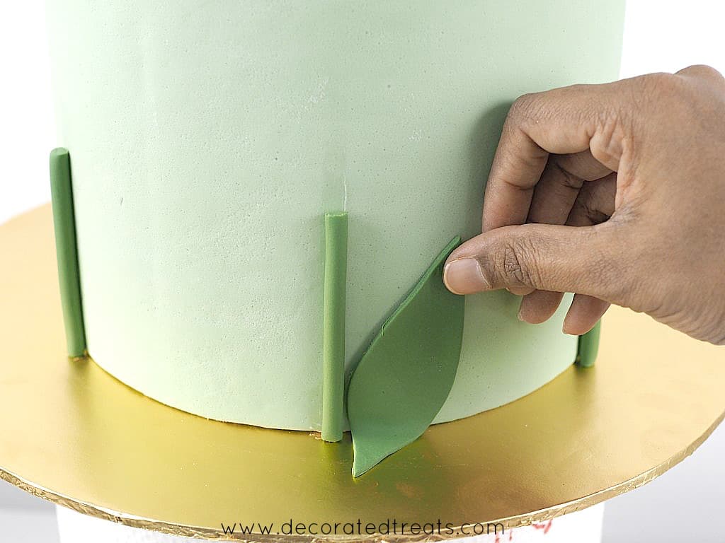 Attaching a green fondant leaf to the side of a cake.