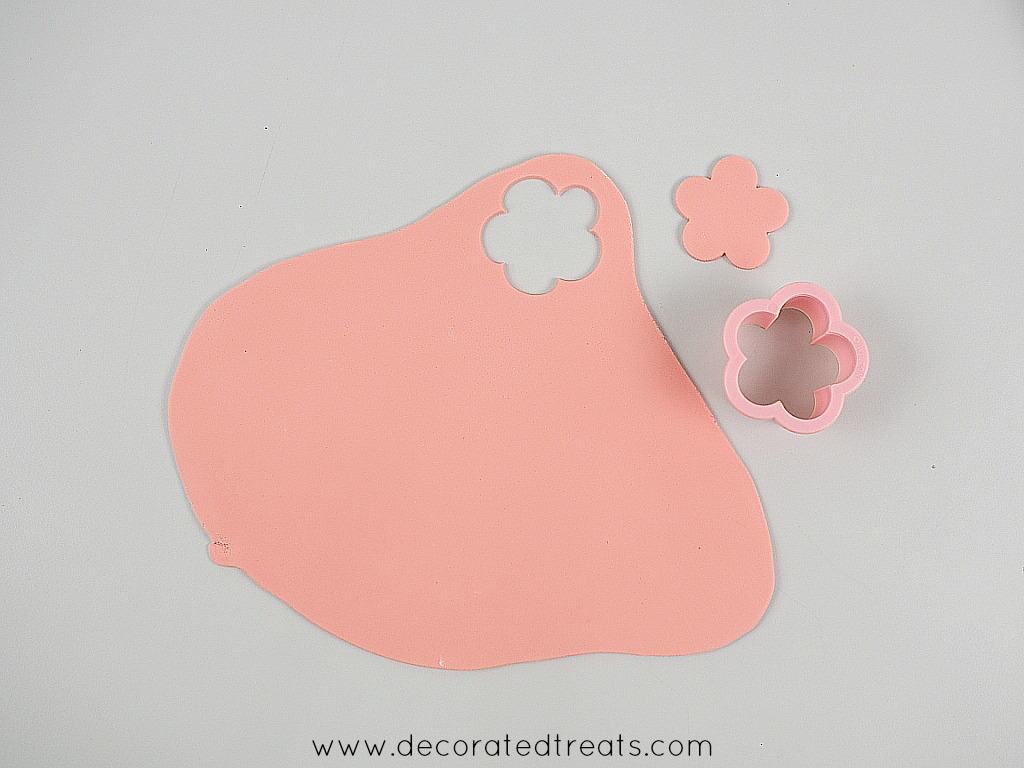 A 5 petal flower cut out of pink fondant. Next to it is the flower cutter