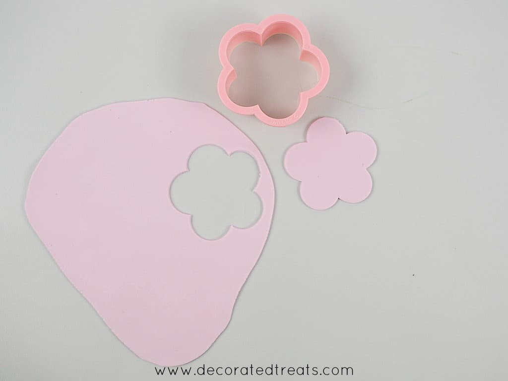 A 5 petal flower cut out of purple fondant. Next to it is the flower cutter.