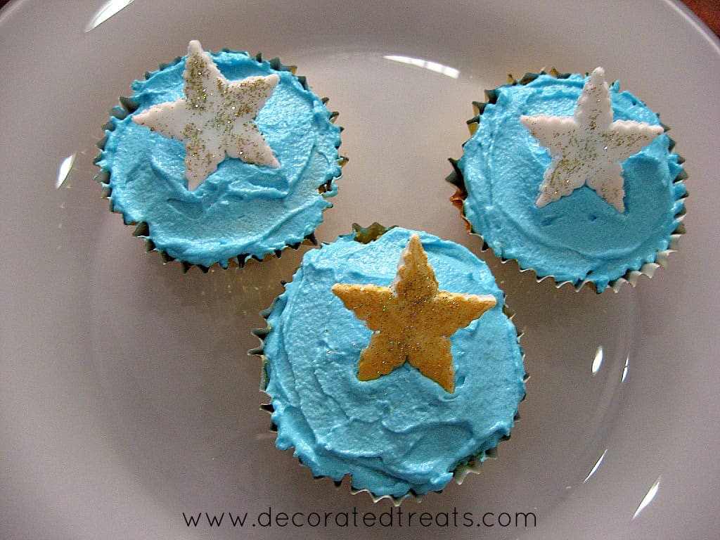 3 cupcakes covered in blue icing and white and gold stars