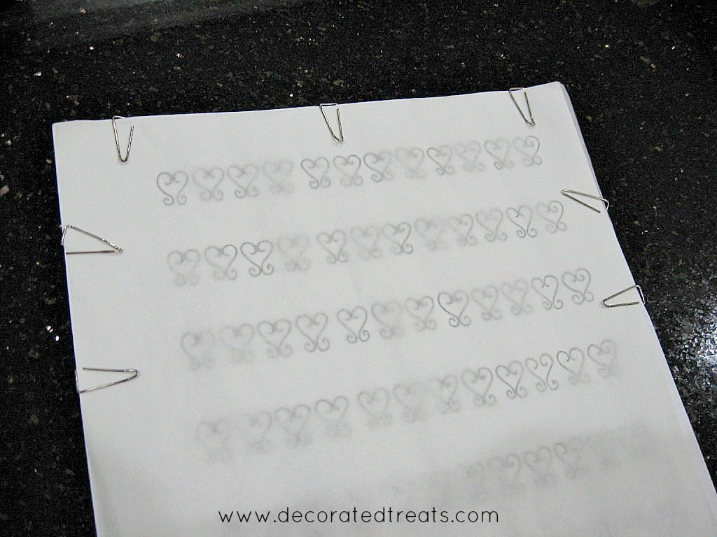 A see through paper on a piece of filigree design template, secured with paper clips