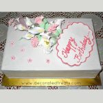 A rectangle cake with a bouquet of gum paste flowers on it and a fondant plaque.