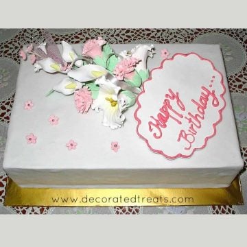 A rectangle cake with a bouquet of gum paste flowers on it and a fondant plaque
