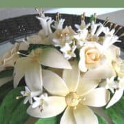 Cream colored gumpaste flowers and green leaves on a cake.