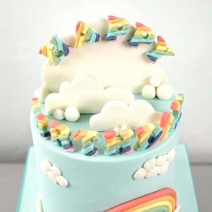 Top of a cake decorated with 3d clouds and rainbow lettering
