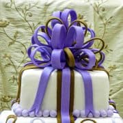 A violet and brown fondant loop bow on top of a 2 tier square cake.