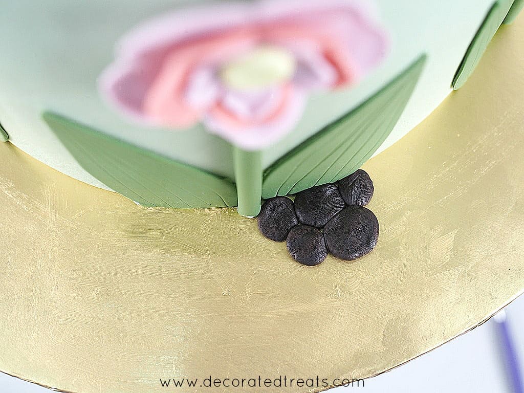 5 small pieces of flat, brown fondant on a gold cake board