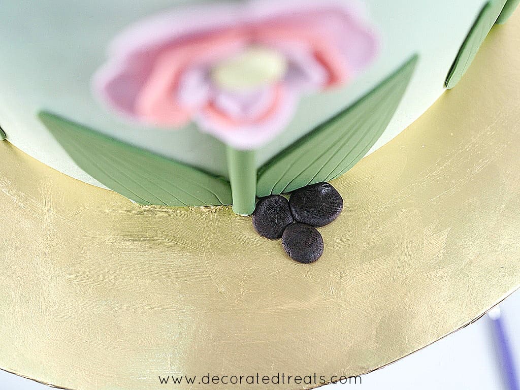 3 small pieces of flat, brown fondant on a gold cake board