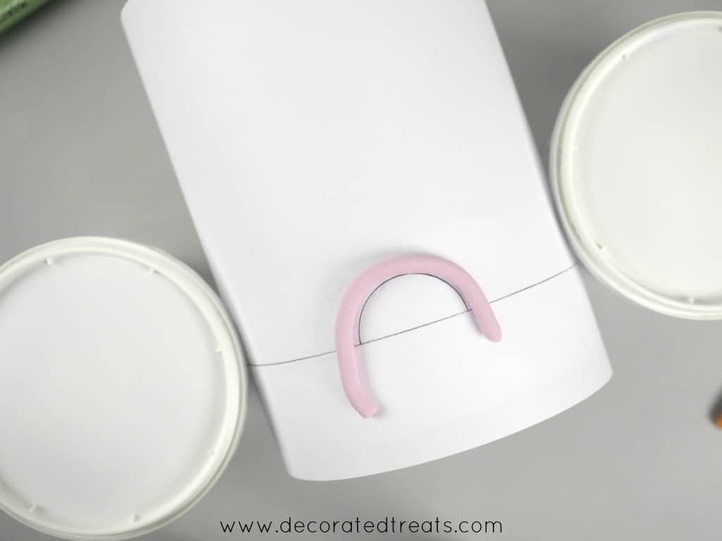 A violet strip of fondant in a semi circle position on a paper template around a styrofoam dummy.