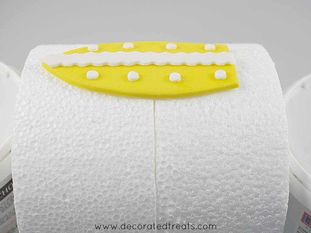 Yellow fondant surf board with white polka dots, on the sides of a styrofoam dummy