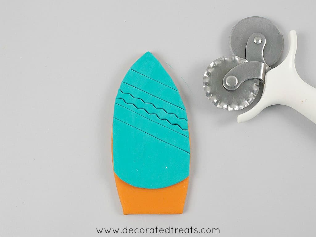Fondant cut out in the shape of a surfboard in orange with blue stripes