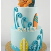 A poster of 4 fondant surf boards and a 2 tier cake decorated with hibiscus and fondant surfboards.