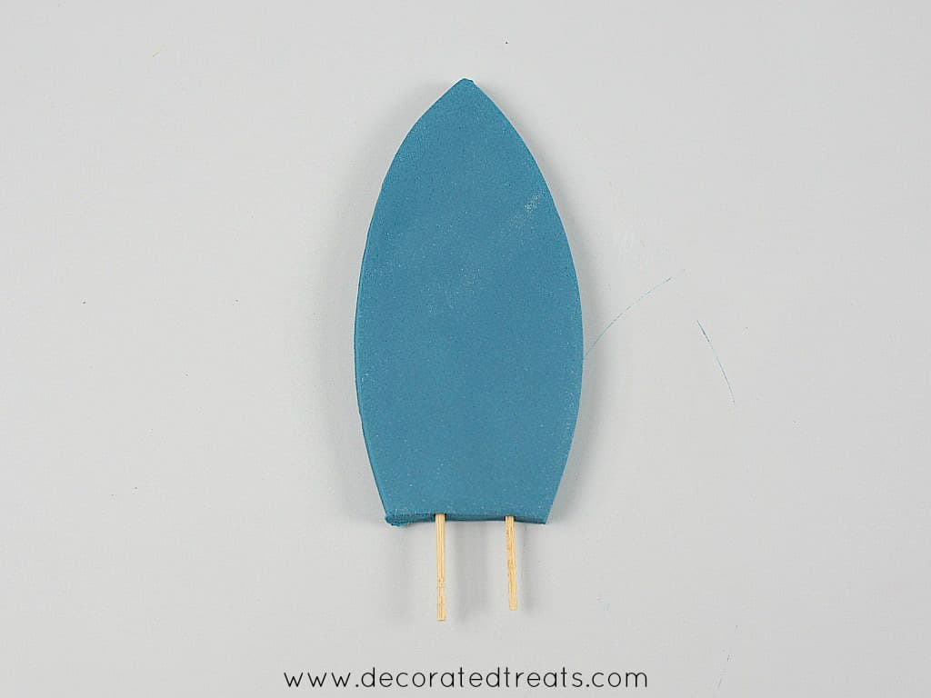 2 toothpicks attached to the bottom of a fondant cut out in the shape of a surf board