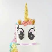A two tier unicorn cake with eyes and golden horn.