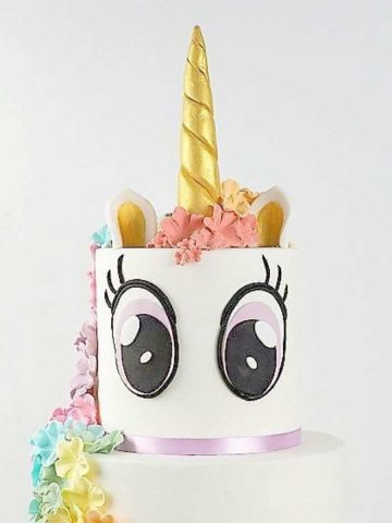 A two tier unicorn cake with eyes and golden horn.