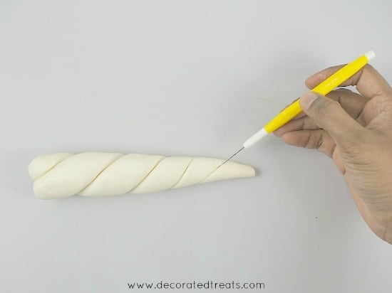 Using a needle tool to draw the lines on a fondant unicorn horn