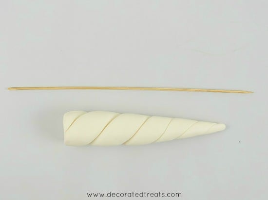 A white fondant unicorn horn with a long pick next to it