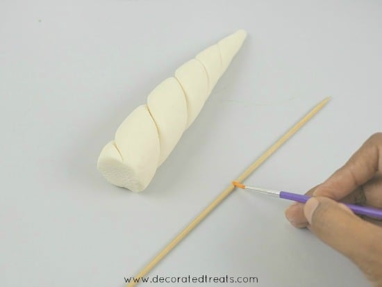 Applying glue to a long pick with brush. Next to it is a fondant unicorn horn.