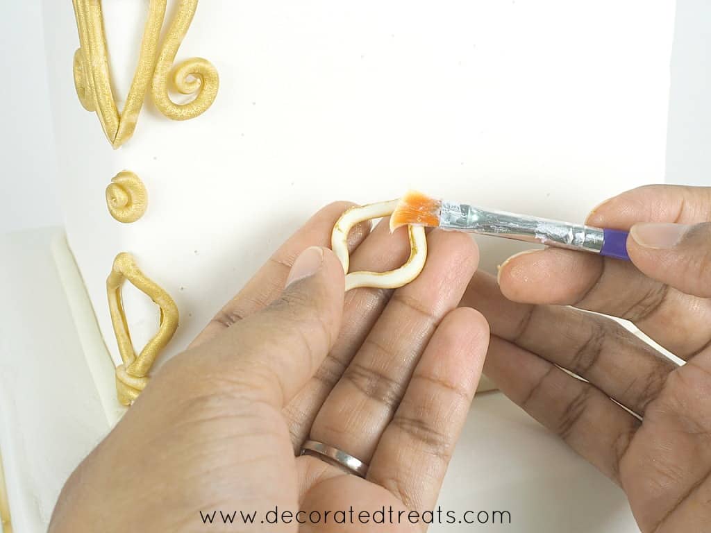 Applying glue to fondant lace pieces with a brush.