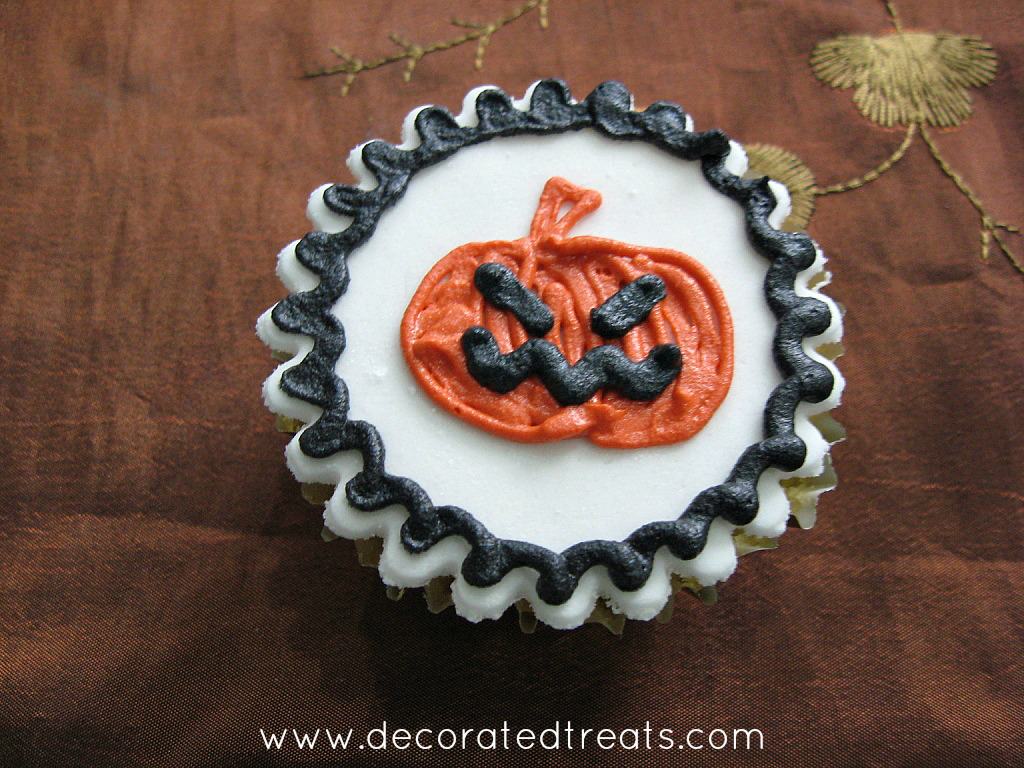 A cupcake decorated with an orange Halloween pumpkin design