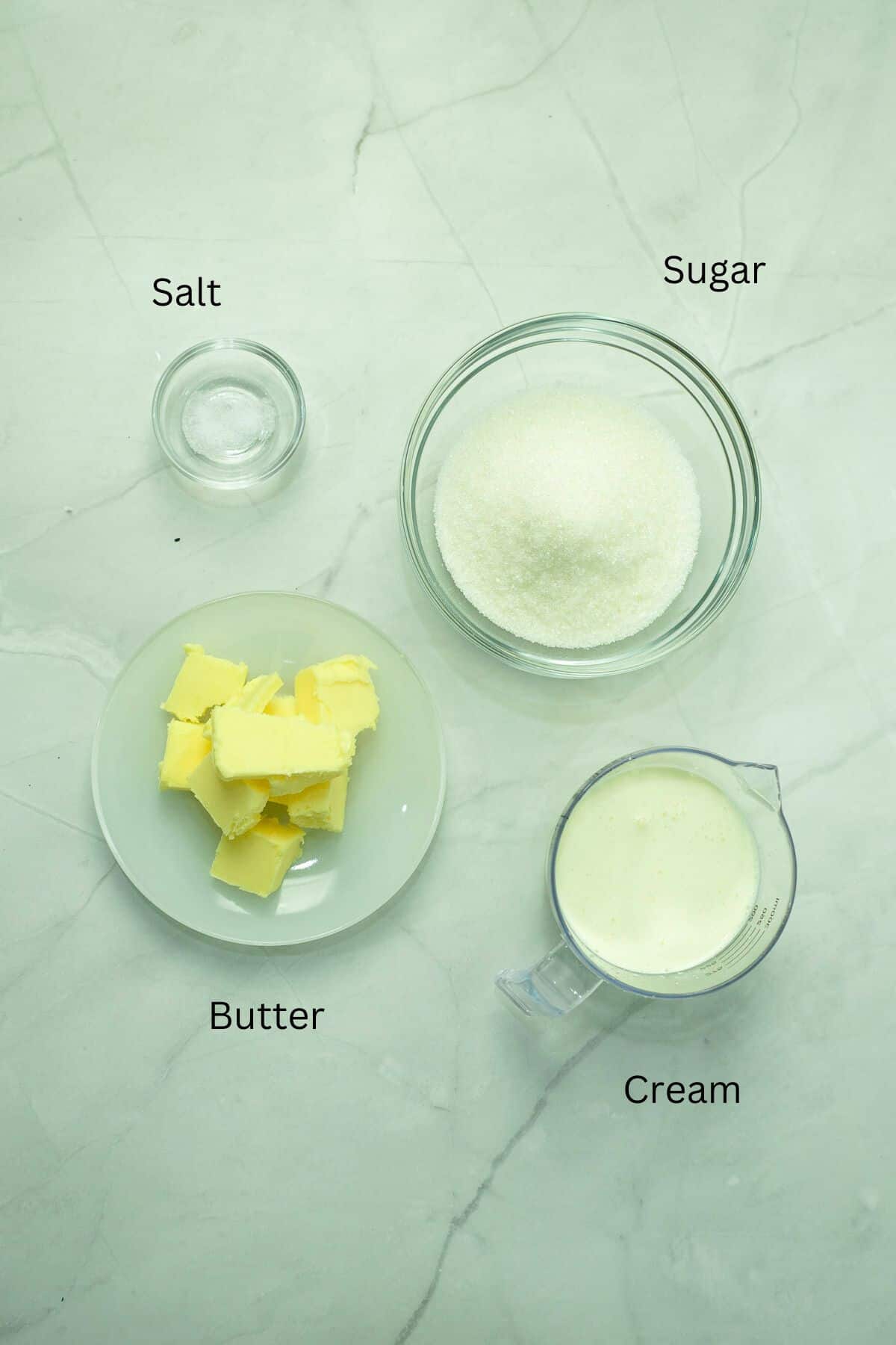 Salt, butter, sugar and cream against a marble background.