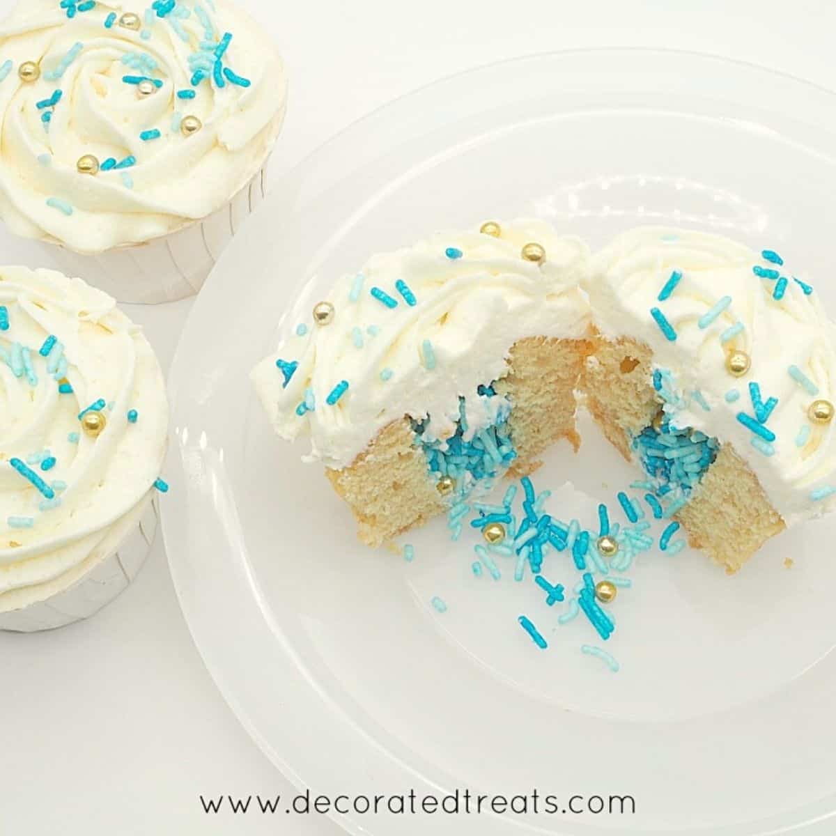 A cupcake on a white plate, cut into half with sprinkles flowing out.