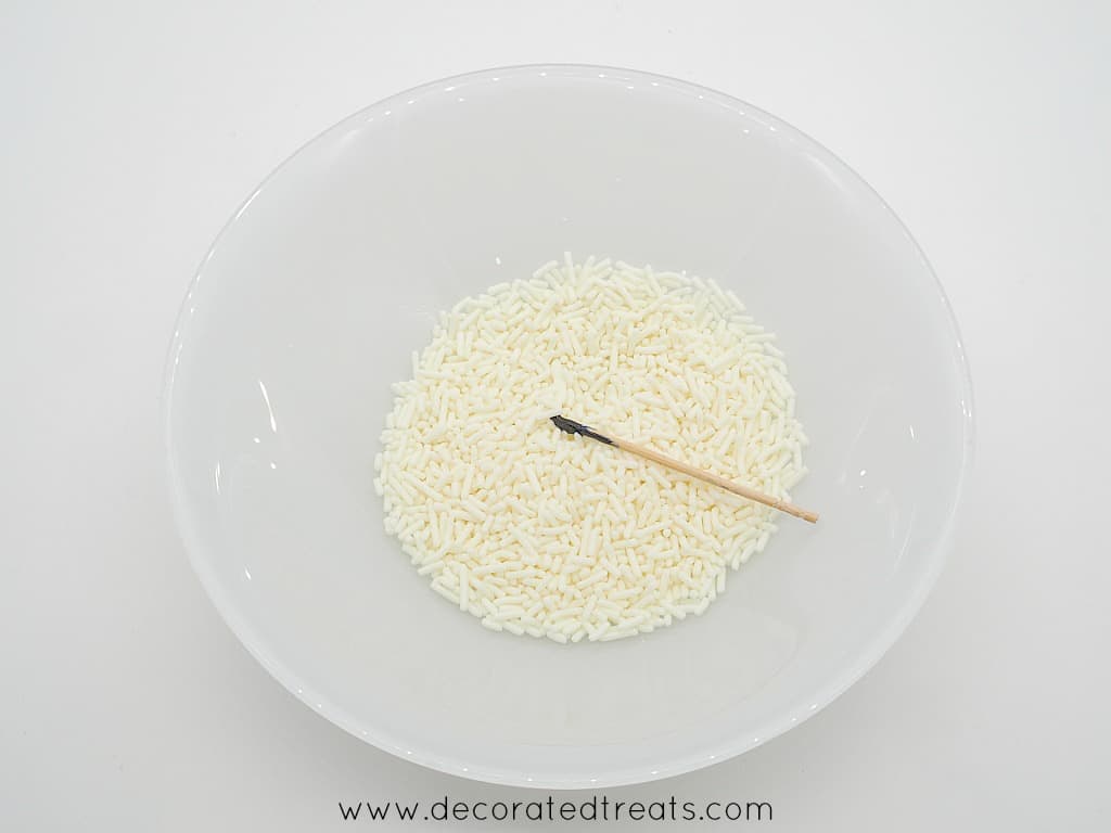 White sprinkles in a white plate with a food coloring dipped toothpick in it.