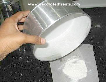 Tapping off excess flour from a round cake tin onto a parchment paper