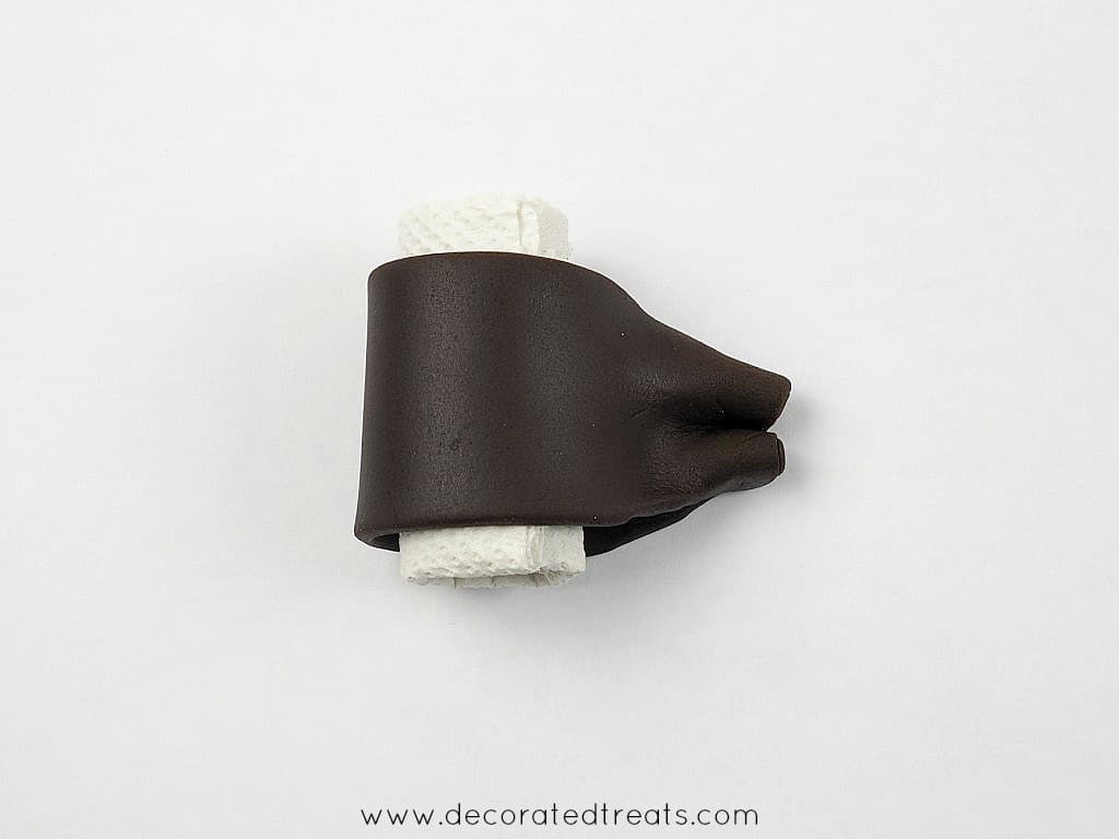 A strip of brown fondant wrapped around a small roll of tissue and the edges gathered