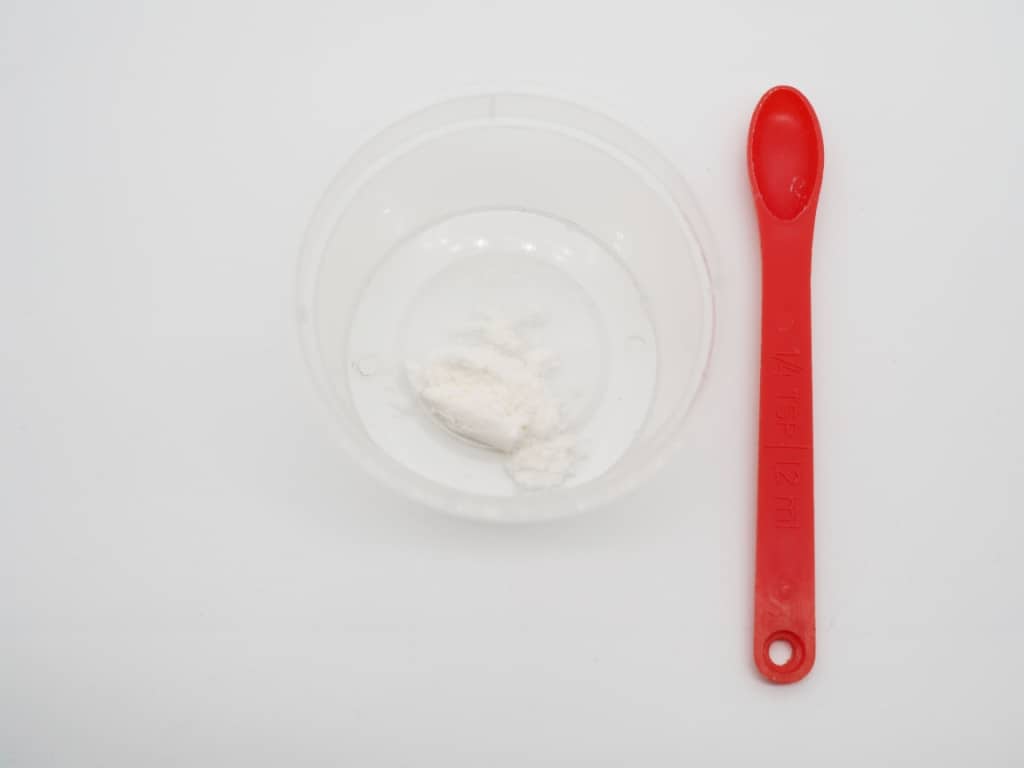 A small red measuring spoon next to a small container of water and CMC