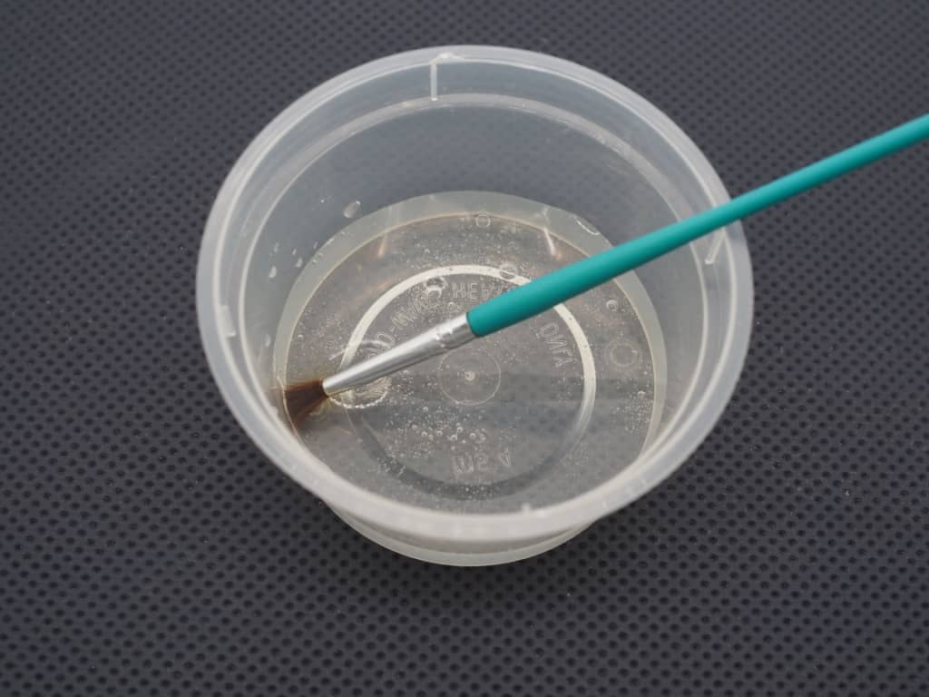 A container of clear fondant glue with a green brush in it